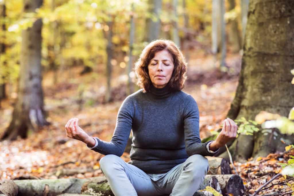 mid-aged woman sitting on a log in the woods meditating