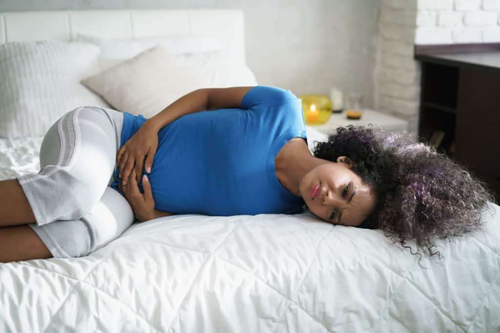 Sad young latina woman with abdominal pain lying on bed at home